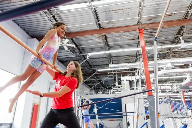 Child working with coach on the bars in gymnastics class at Dominique Dawes Academy