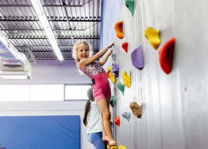 Child climbing rock wall in class at Dominique Dawes Academy