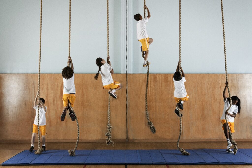 Children climbing ropes in a gym class to build strength and stamina for back to school readiness.