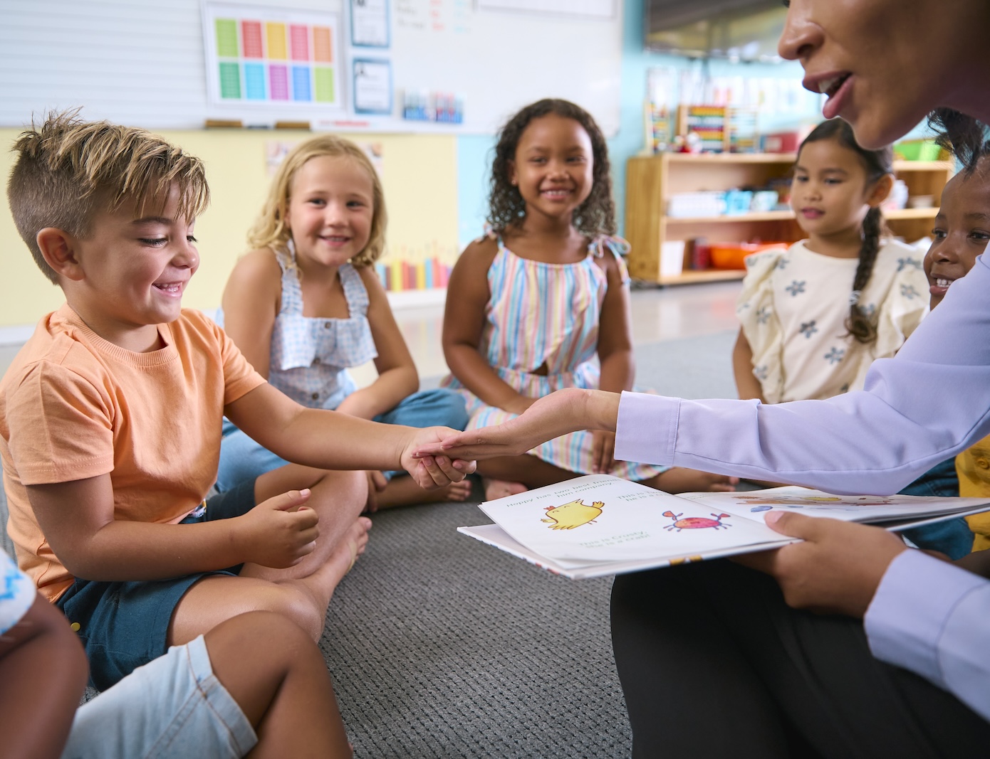 Young children sitting in a circle with their teacher during story time as part of back to school classroom activities.