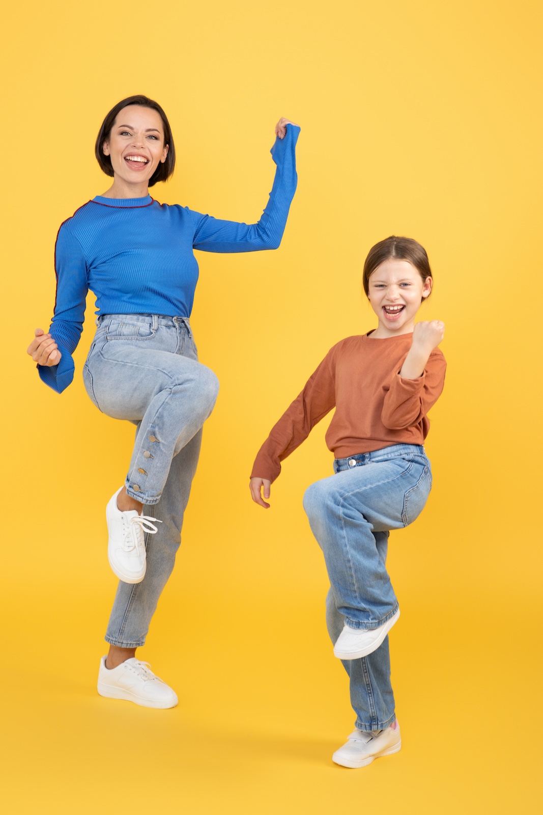 A mother and her daughter dance joyfully against a bright yellow background. They express happiness and affection, showcasing their strong bond through fun and playful movement.