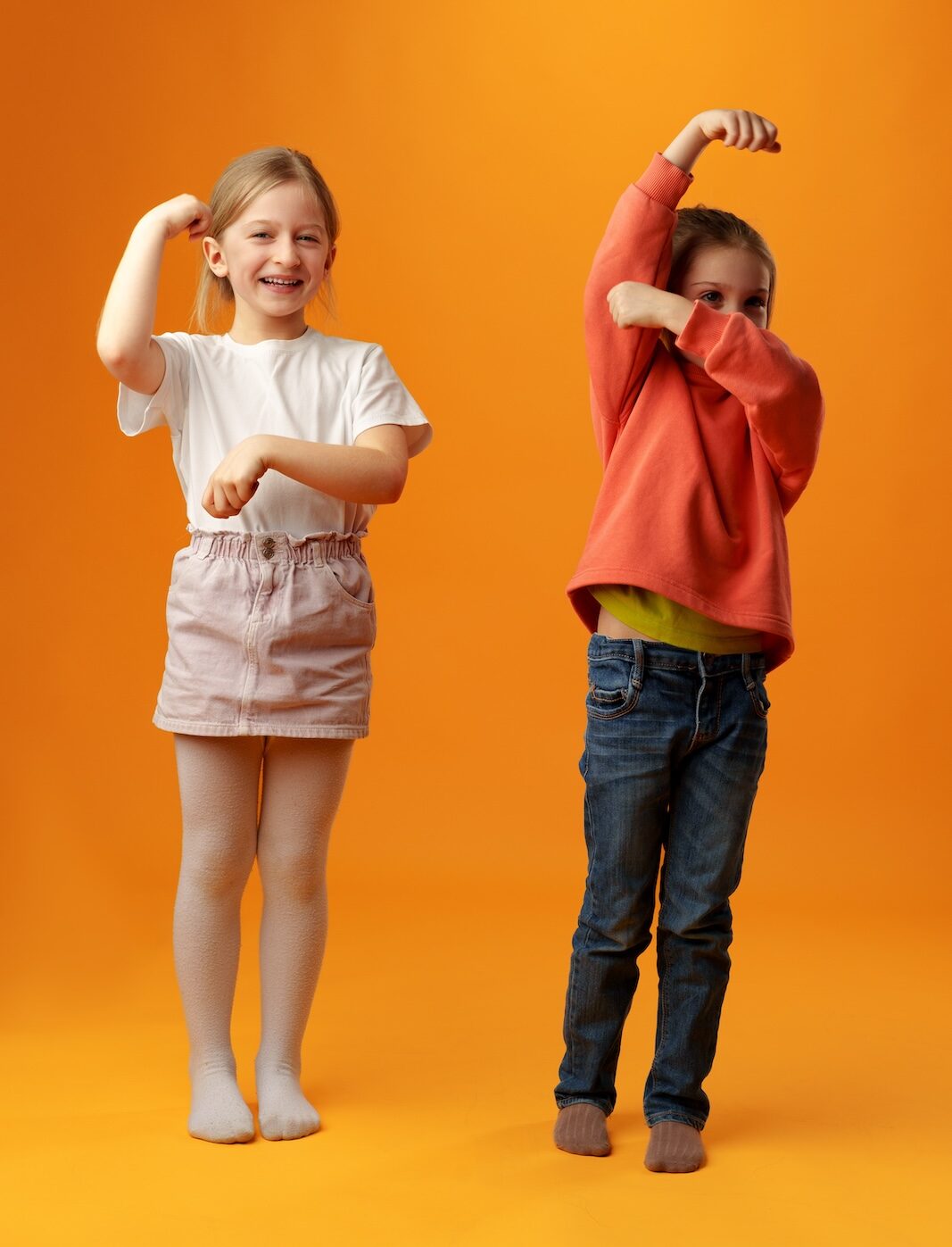Two cute little girls standing on yellow background in the studio
