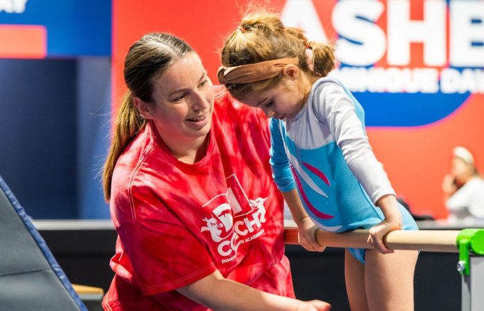 Child learning gymnastics with the help of a coach at DDGNA in Ashburn, VA.