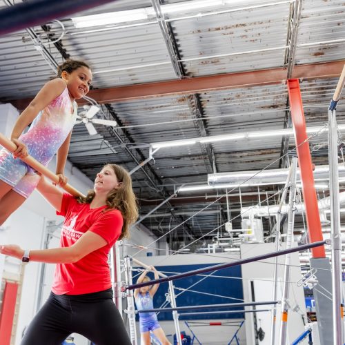 Child working with coach on the bars in gymnastics class at Dominique Dawes Academy