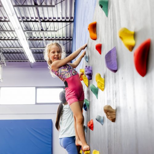 Child climbing rock wall in class at Dominique Dawes Academy