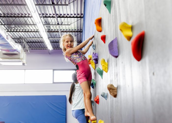 Child climbing rock wall in class at Dominique Dawes Academy