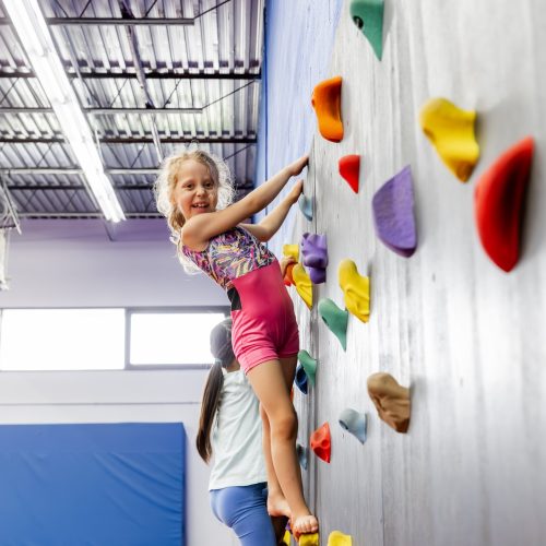 Child climbing rock wall in class at Dominique Dawes Academy