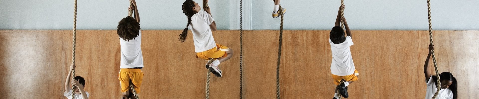 Children climbing ropes in a gym class to build strength and stamina for back to school readiness.